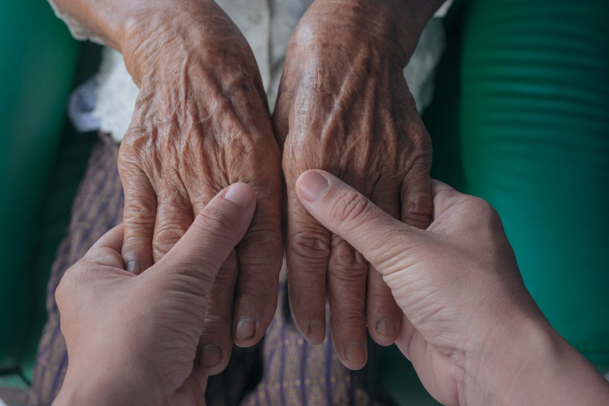 A younger person holding the hands of an elderly woman